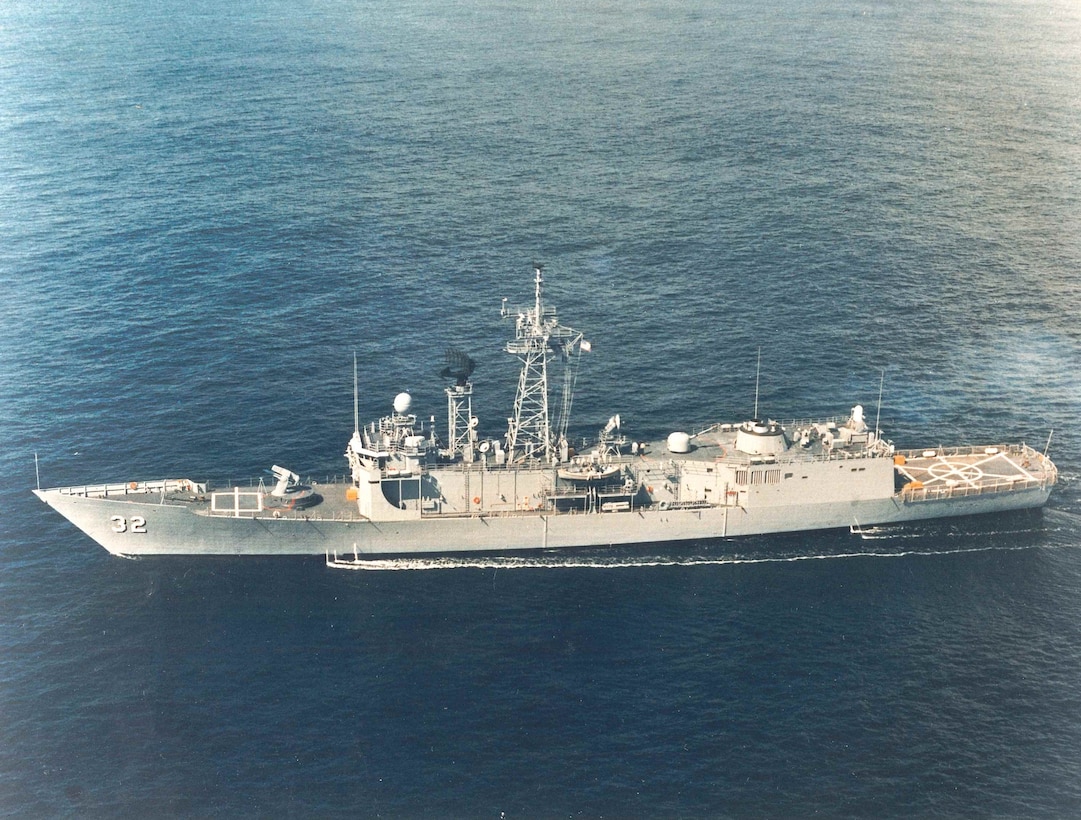 A colored photograph, taken off the warship’s port side, shows the newly-commissioned guided-missile frigate USS John L. Hall (FFG-32) steaming along, circa 1982.