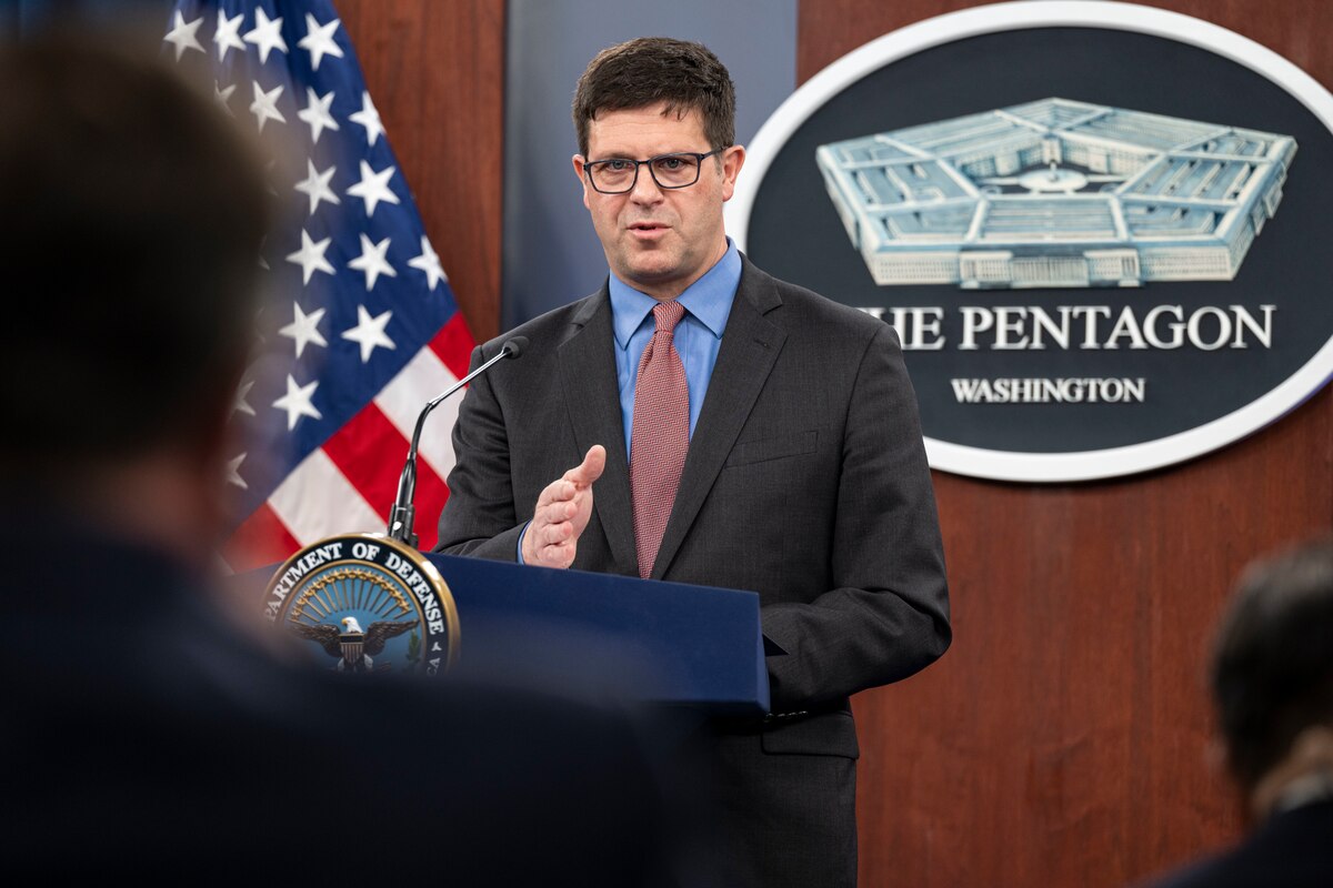 A man wearing a suit gestures with his hand while standing at a lectern.