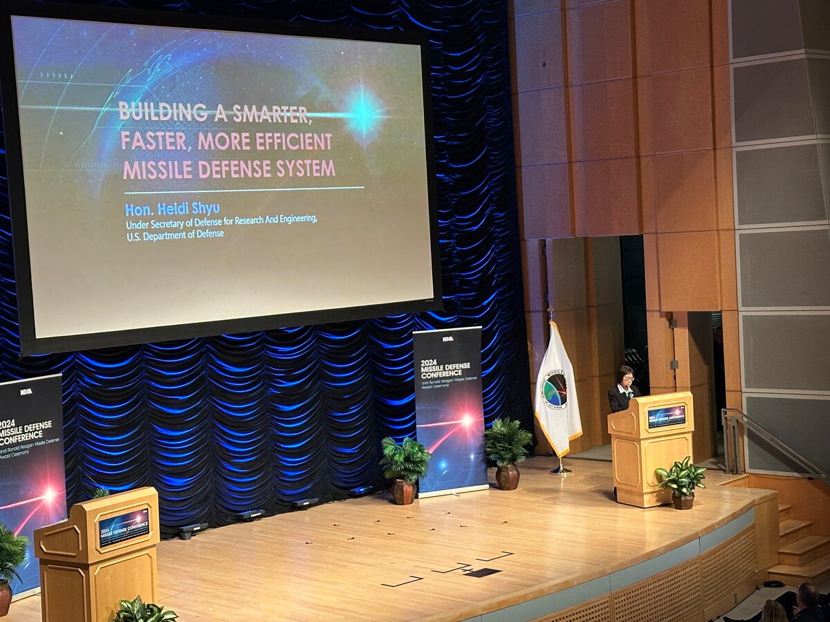 A woman stands at a lectern on a stage.