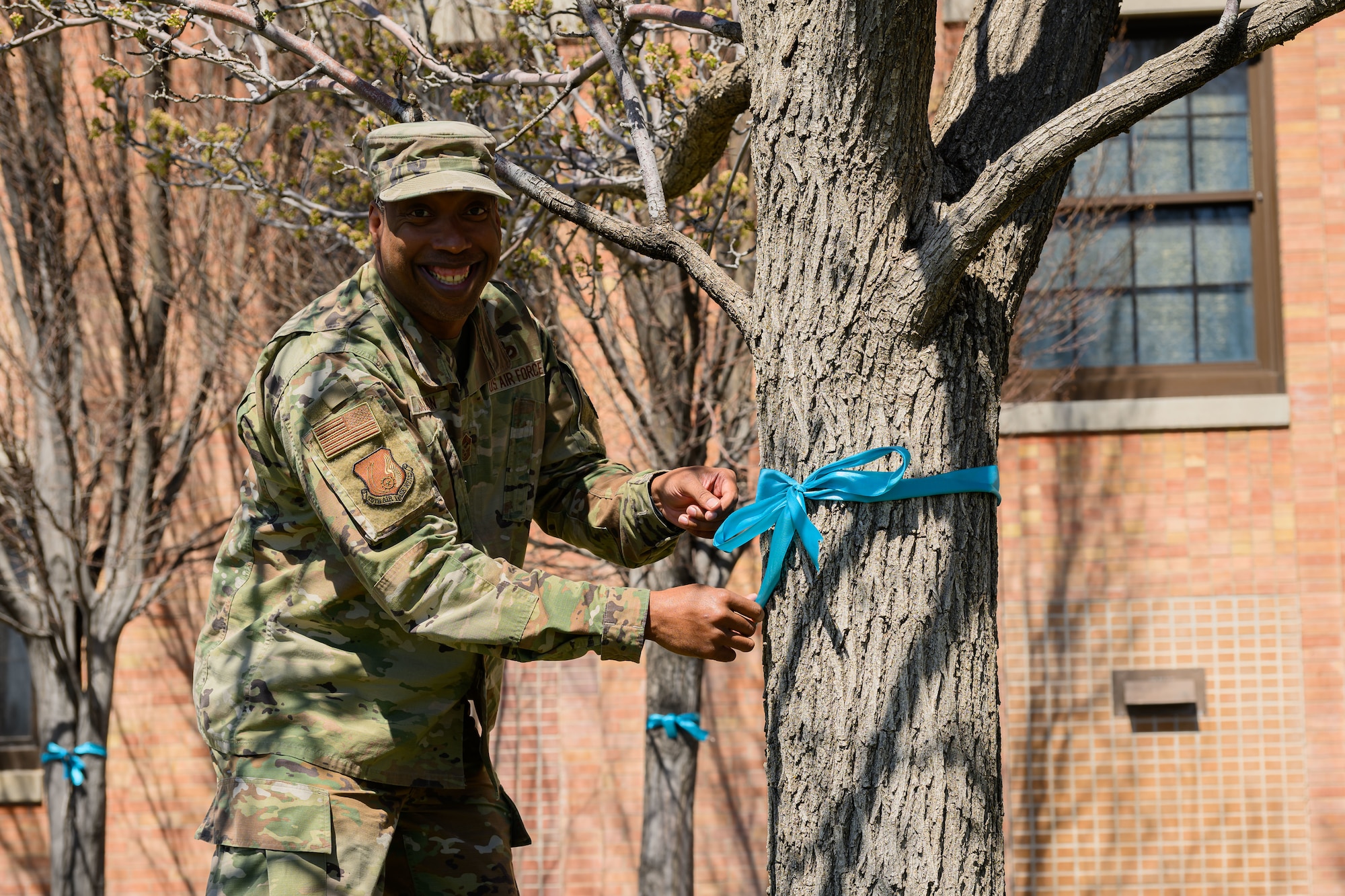 Chief Jackson ties a teal ribbon in a bow around the trunk of a tree.