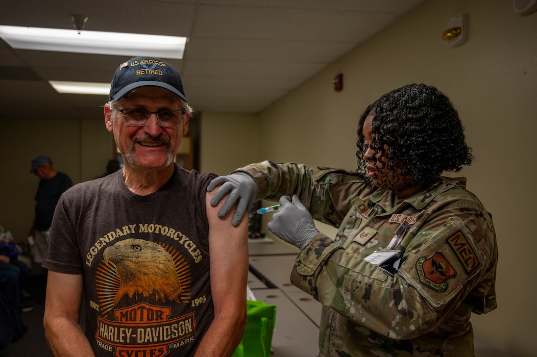 Retired U.S. Air Force Tech Sgt Dennis Nowak (left) receives a vaccine from Staff Sgt Kapries Chaplin (right), 56th Medical Group allergy and immunizations technician  and noncommissioned officer in-charge, during a retiree appreciation event October 21, 2023, at Luke Air Force Base, Arizona.