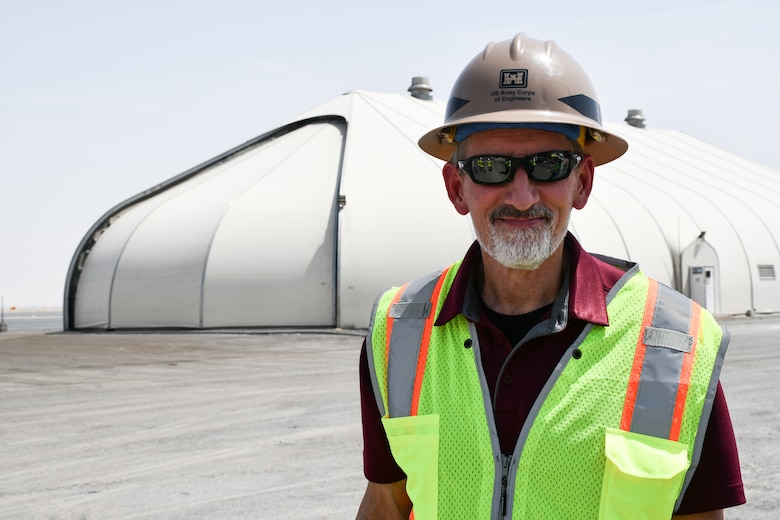 Male civilian engineer stands in front of a structure on a runway that is under construction.