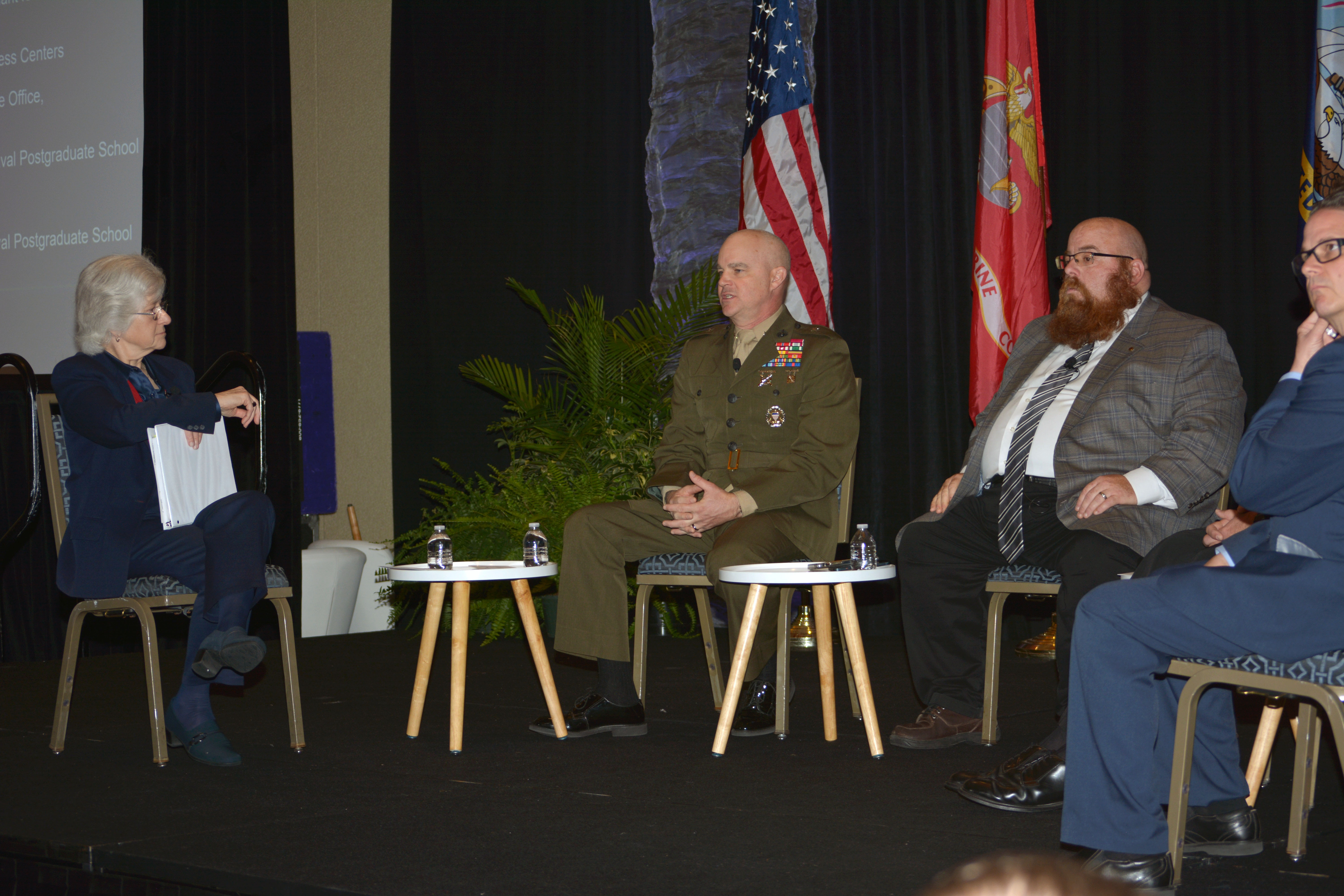 Brig. Gen. Forrest Poole speaking with three other people on a stage, all seated in chairs.