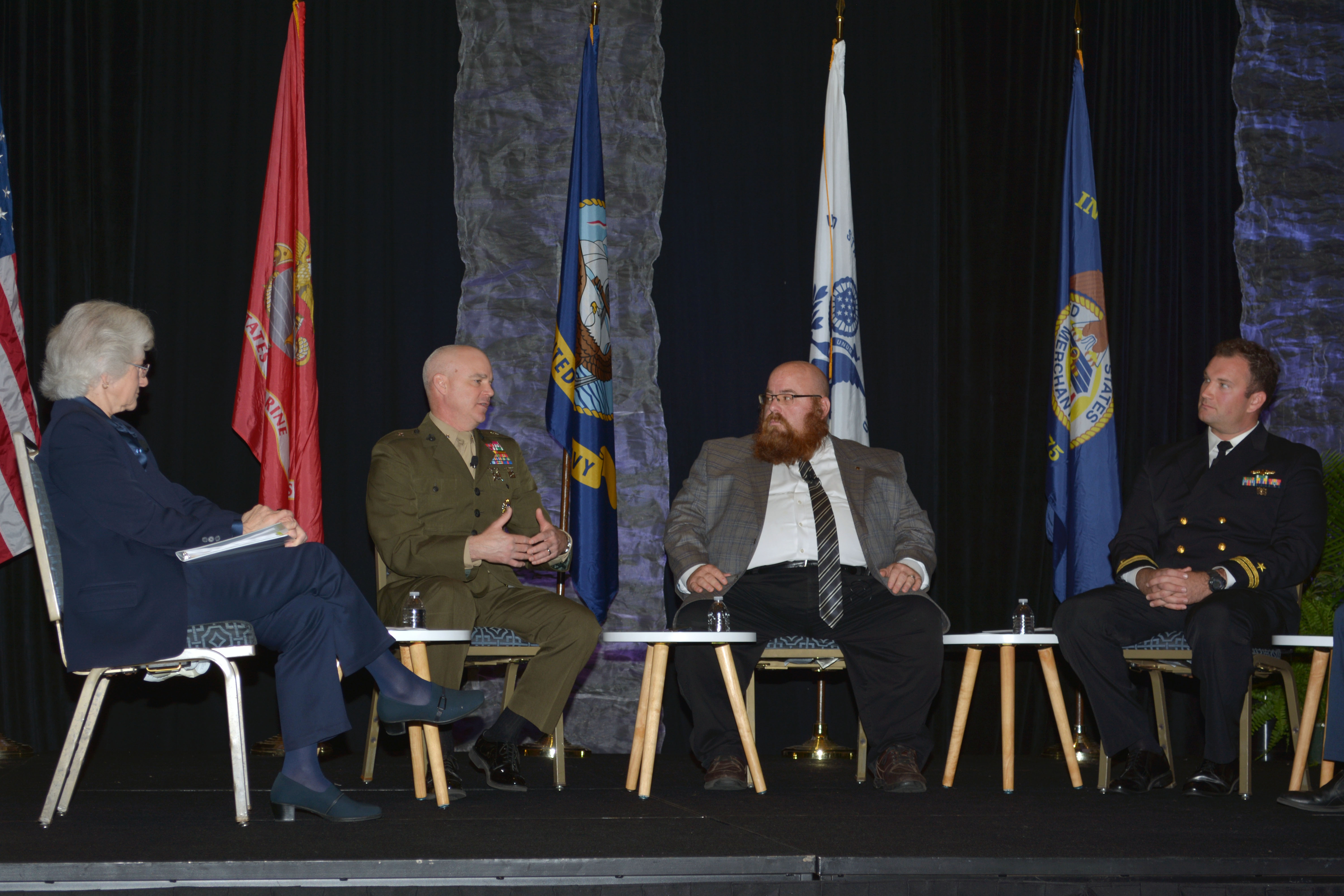 Brig. Gen. Forrest Poole speaking with three other people on a stage, all seated in chairs.