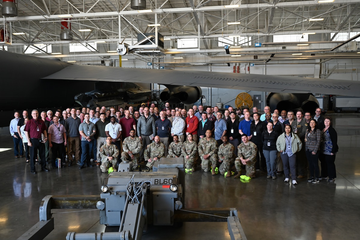 Conference attendees pose for a group photo inside a hangar, with a B-52 in the background.