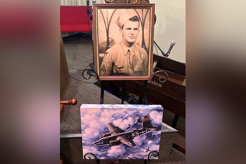 A  black and white photo of an airman sits in a room with other military mementos.