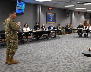 The deputy commander speaks to the council in a large conference room.