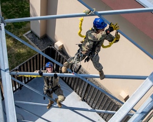 Two military members climb the middle of a tower.