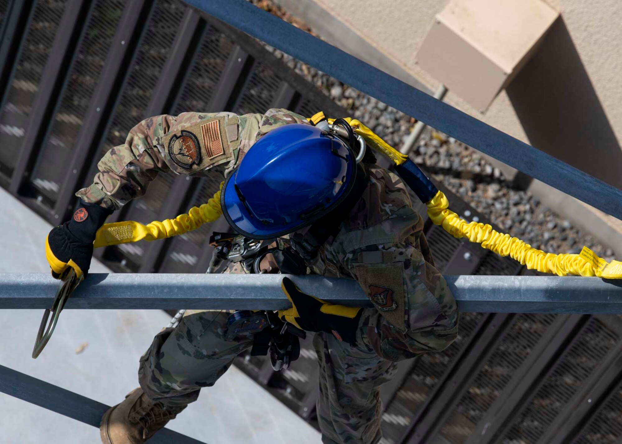 A military member attaches a hook to a tower.