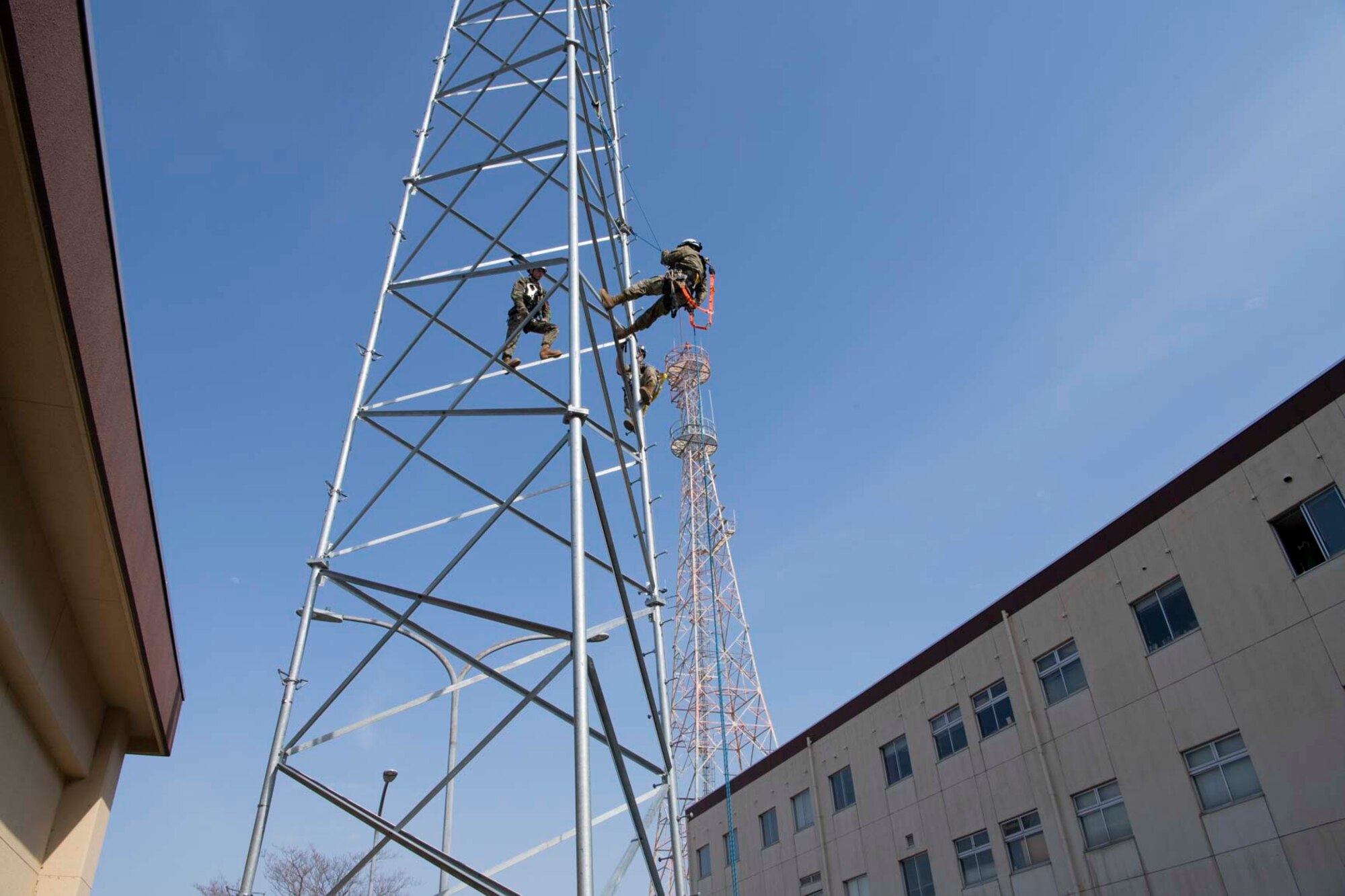 Three military members climb a metal tower.