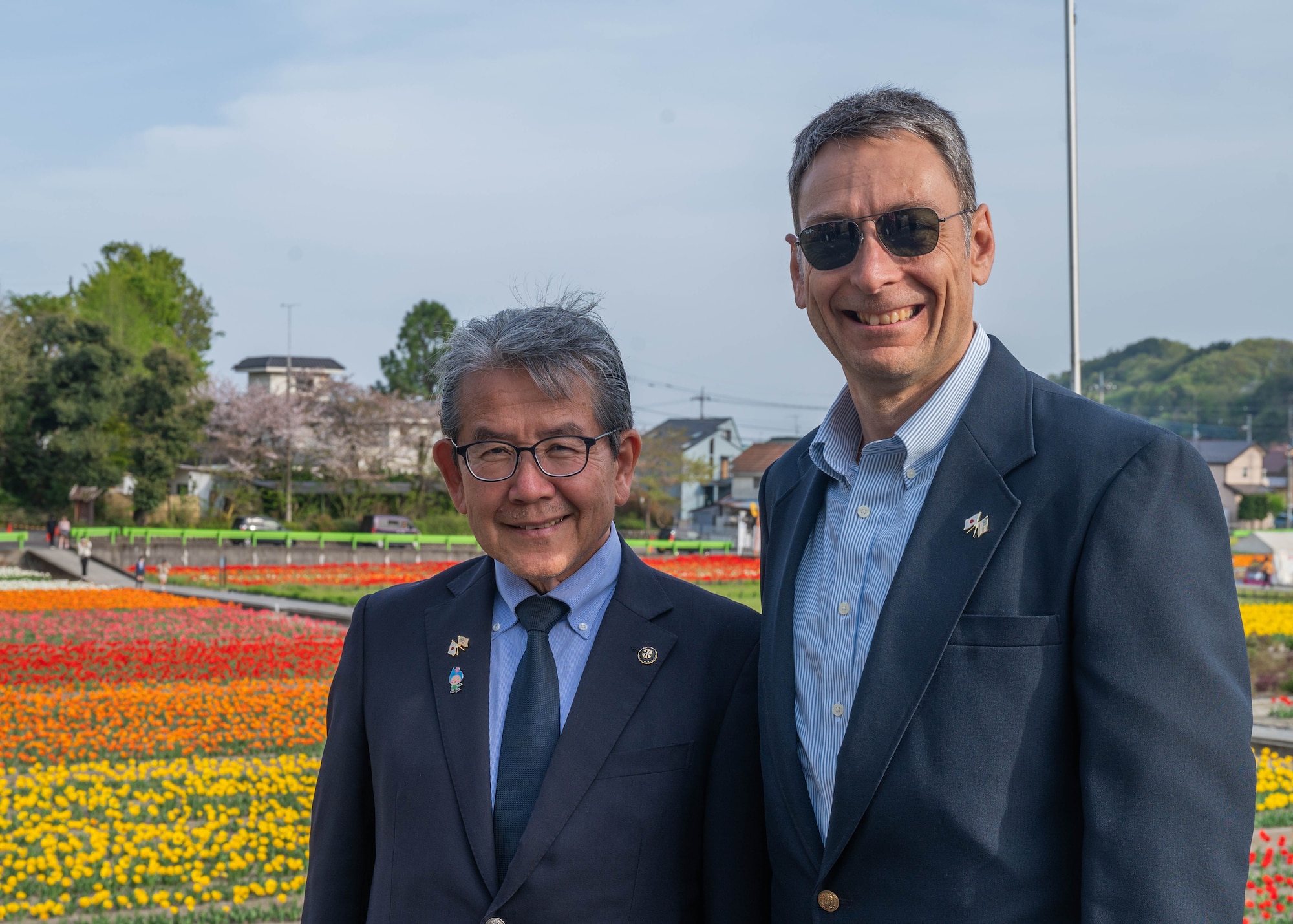 Two men pose for a photo in front of a field of tulips.