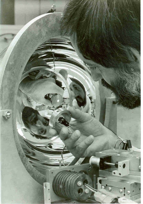 Arnold Engineering Development Center research engineer Bob Wood uses a light source to study a hemiellipsoidal mirror. The apparatus was used to measure infrared reflectance of satellite materials and other hardware exposed to the cold temperatures of space. This image was featured on the frontpage of the February 1982 issue of High Mach. (U.S. Air Force photo)