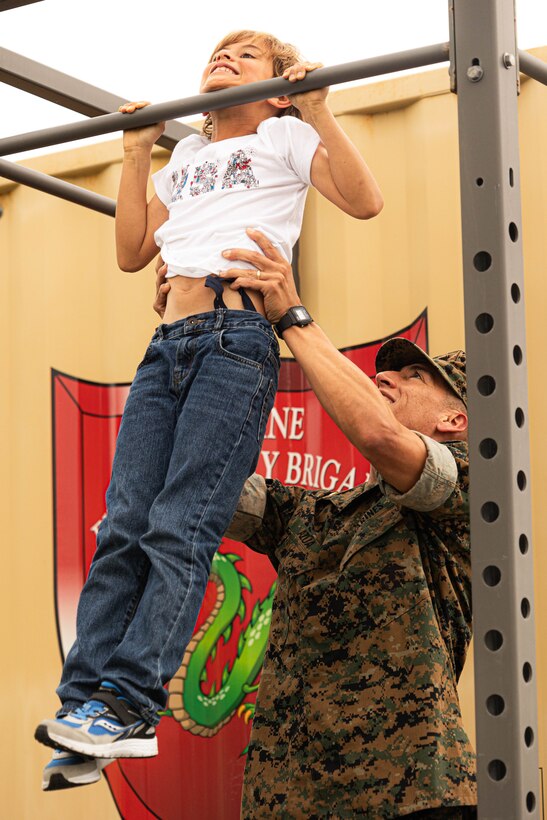 Maj. Marcos Azua, the comptroller for the 3rd Marine Expeditionary Brigade, helps his son, Martin, do pull-ups on Camp Courtney, Okinawa, Japan, April 12, 2024. The Month of the Military Child, celebrated annually in April, recognizes military children for the daily sacrifices and challenges they overcome. (U.S. Marine Corps photo by 1st Lt. Samuel H. Barge)