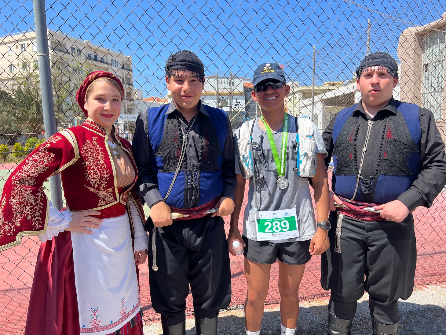 Builder Constructionman David Hutchinson (second from right), assigned to Naval Facilities Engineering Systems Command, Europe, Africa, Central, poses with traditional Cretan dance performers after running 26.2 miles to complete the Crete Marathon in Chania, Crete, Greece on April 14, 2024.