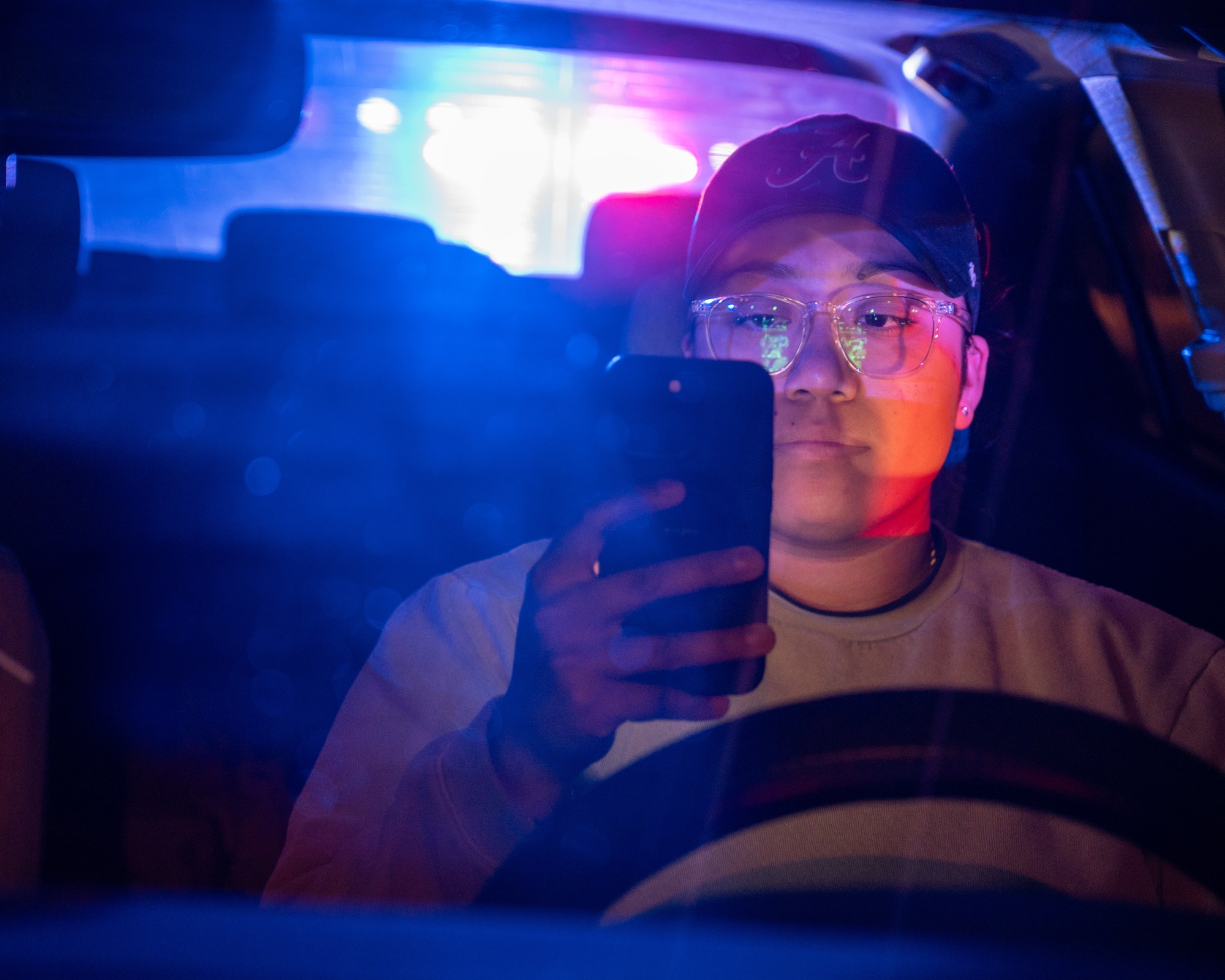 U.S. Air Force Staff Sgt. Siree Contreras, 47th Security Forces Squadron (SFS) noncommissioned officer in charge of police services, holds a phone while in her vehicle with flashing police car lights in the rear window at Laughlin Air Force Base, Texas, April 4, 2024. Distracted Driving is one of the major causes of accidents in the U.S. with 487 fatalities and 2624 serious injuries in Texas during 2022. (U.S. Air Force photo by Staff Sgt. Nicholas Larsen)