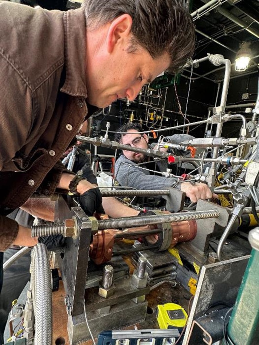 Edgar Felix, Lead Investigator, front and Isaiah Jaramillo, Mechanical Specialist, work on the first-ever, single-block rocket-engine thrust chamber additively manufactured using a process called laser powder directed energy deposition, or DED. DED is an additive manufacturing process in which the device injects metal powder into focused beams of high-power laser in highly controlled atmospheric conditions (U.S. Air Force photo)