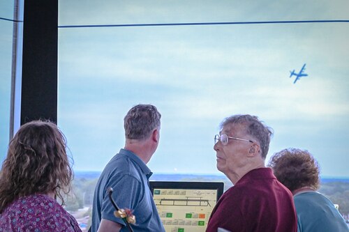 People watch as aircraft fly around a control tower