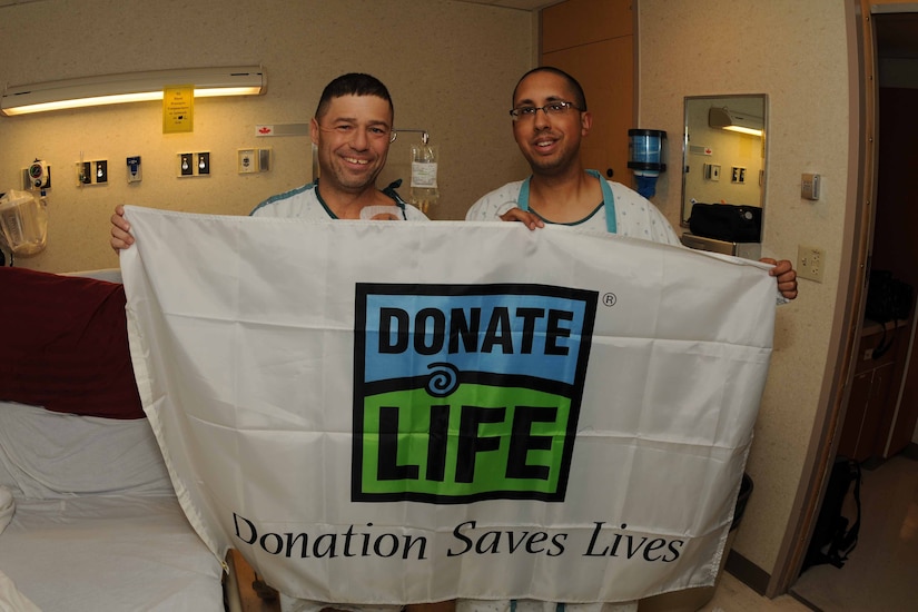 Two men in a hospital room hold up a sign that says, “Donate Life.”