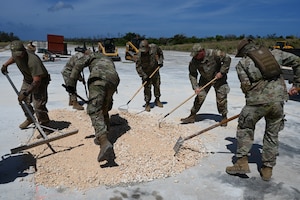 Airmen use large rakes to spread crushed stones into the crater.