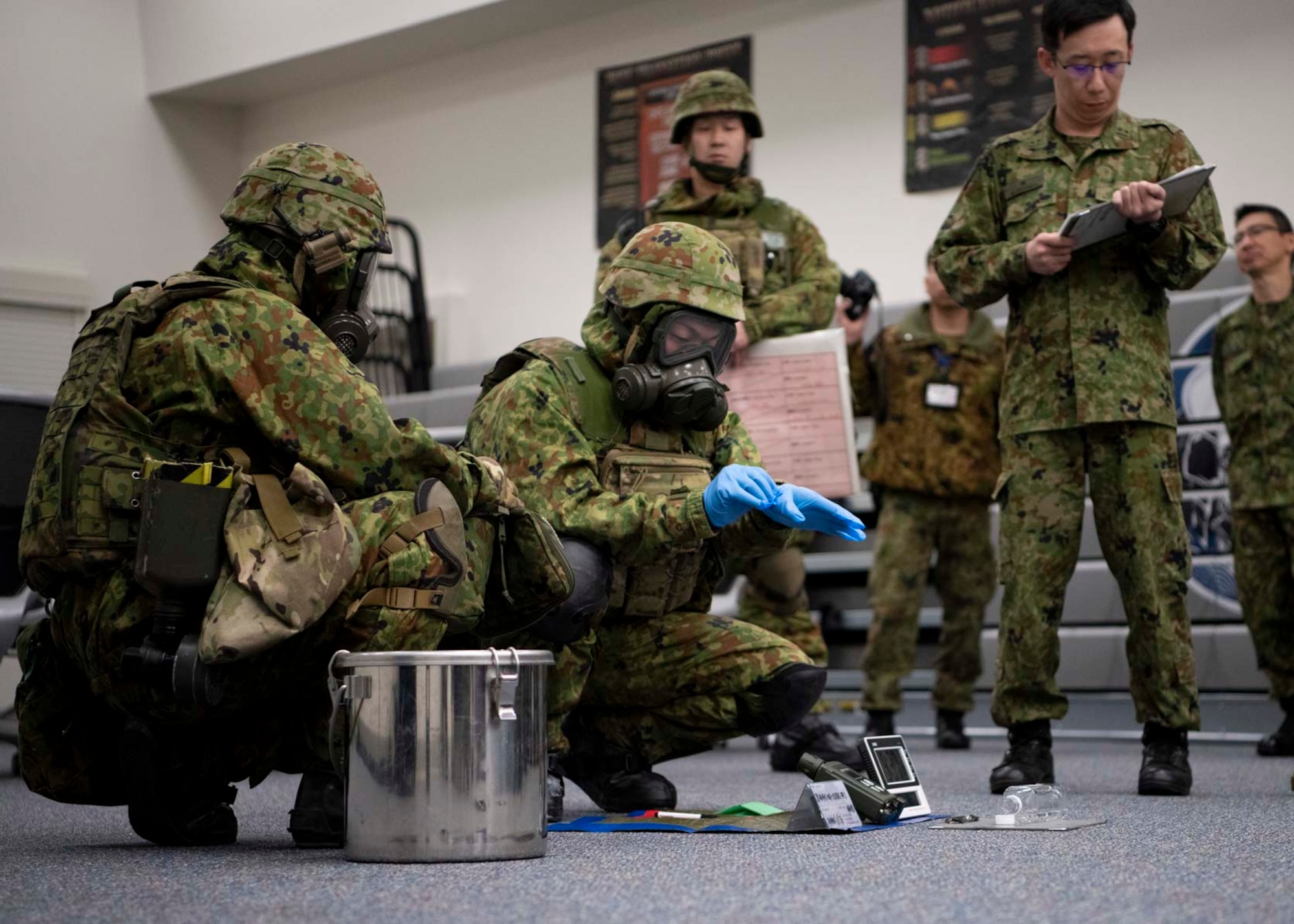 Two Japanese military members crouch down to perform a CBRN demonstration.
