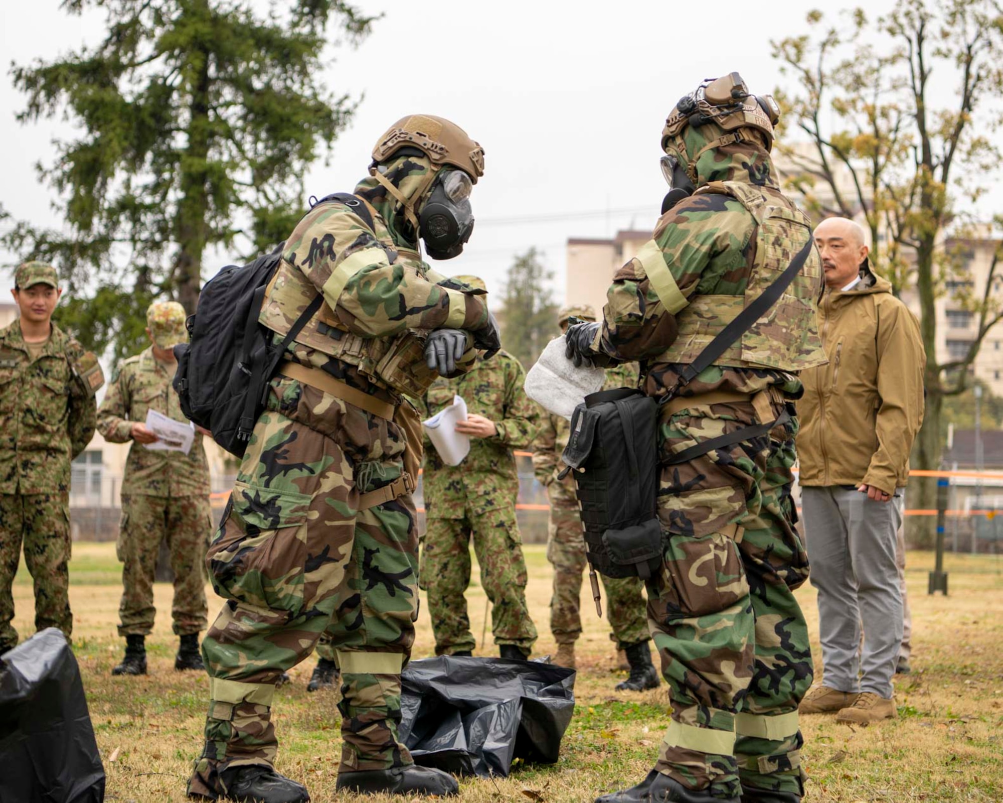 Two U.S. military members in MOPP gear look at a paper.