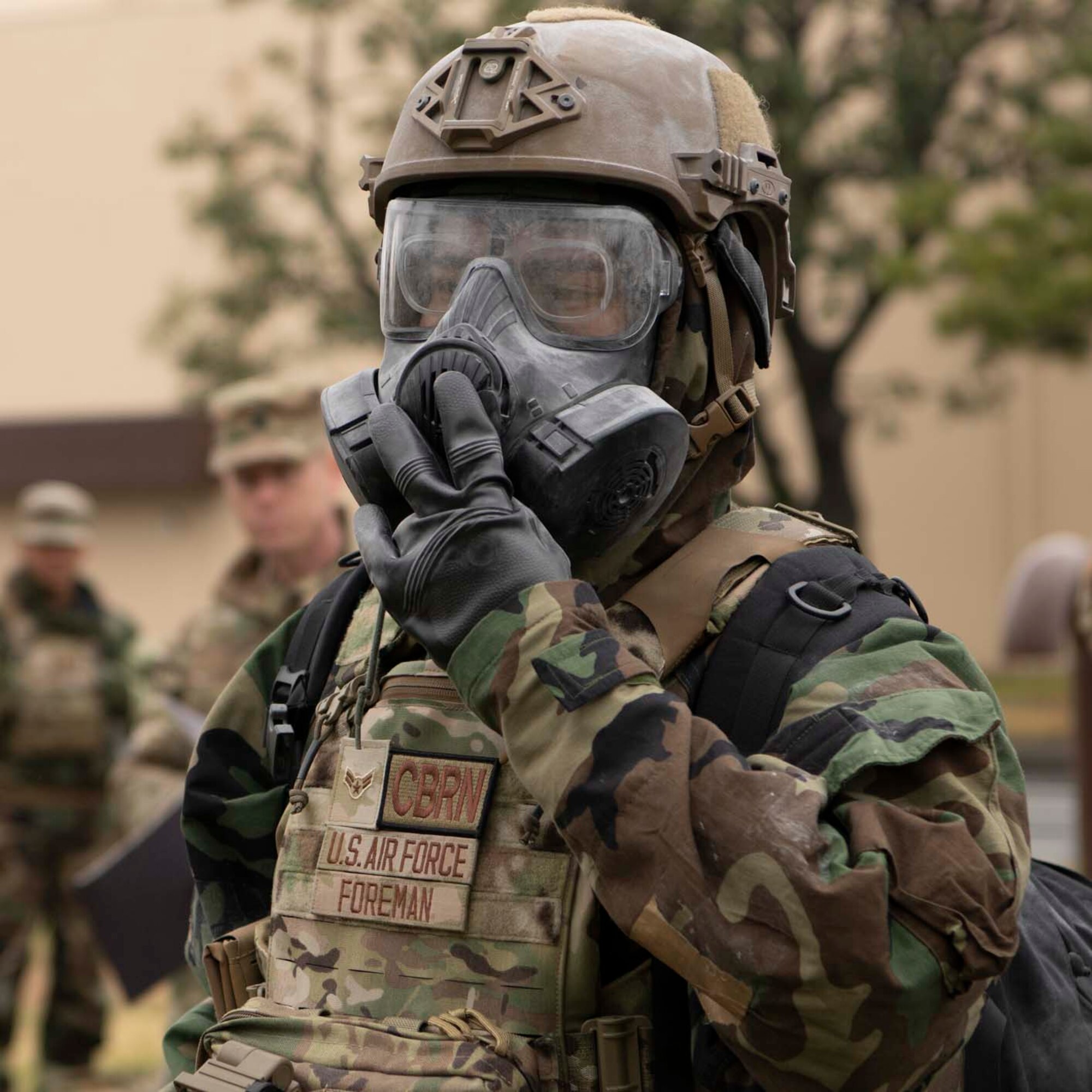 A U.S. miltary member wearing MOPP gears holds on to the front of his mask.