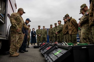 A group of Japanese military members and U.S. military firefighters look at toolboxes lying on the ground.