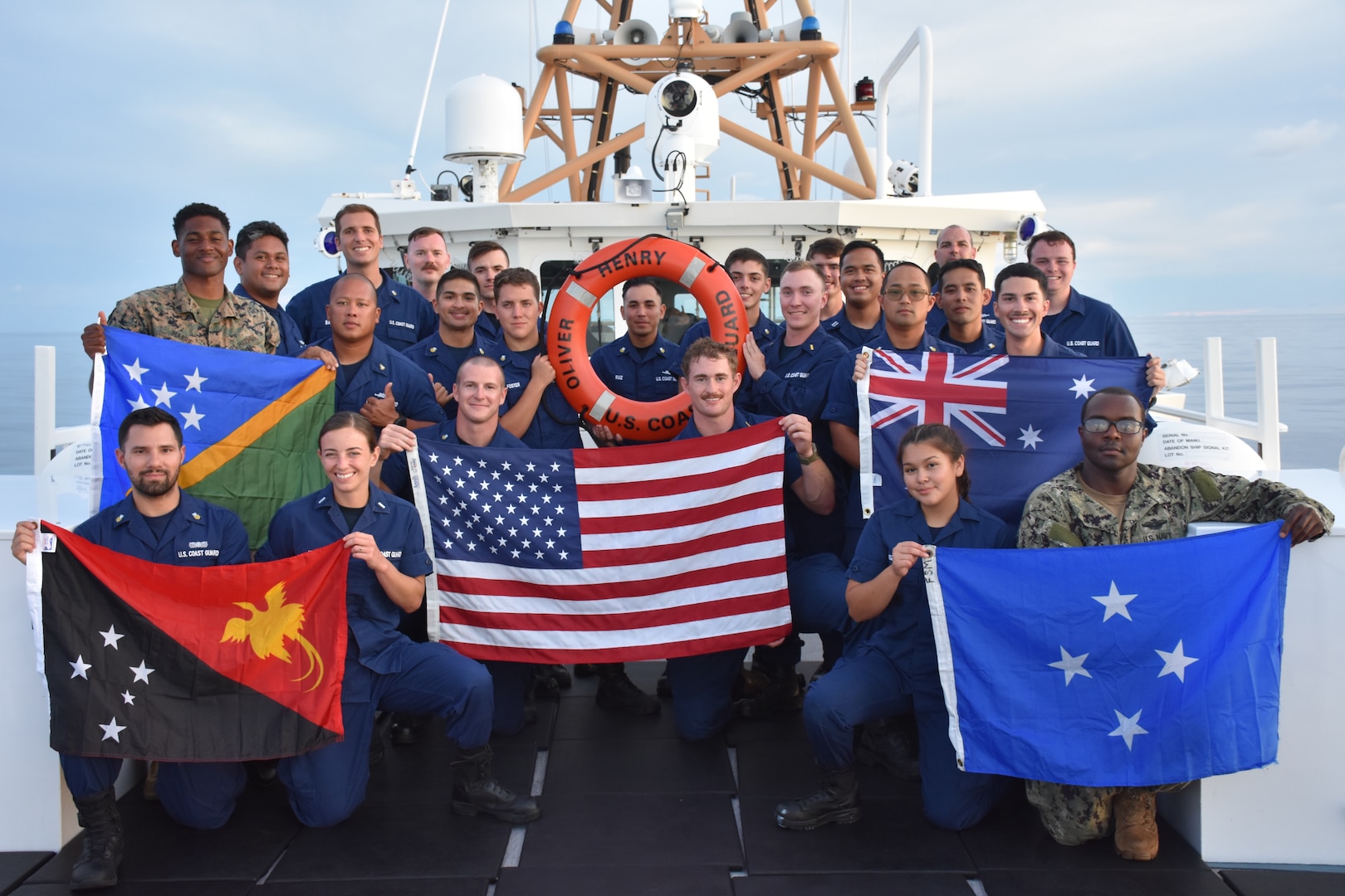 The crew of the USCGC Oliver Henry (WPC 1140) stand for a photo with the flags of all the countries ports and waters they reached during their 2022 expeditionary patrol while at sea in the Pacific on Aug. 12, 2022. They conducted a historic expeditionary patrol across Oceania, covering more than 8,000 nautical miles from Guam to Australia and return with several stops in Papua New Guinea and one in the Federated States of Micronesia. (U.S. Coast Guard photo)