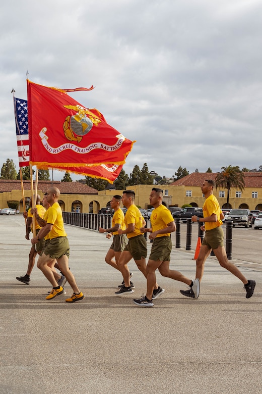 Marine Corps recruits carrying flags run in formation.