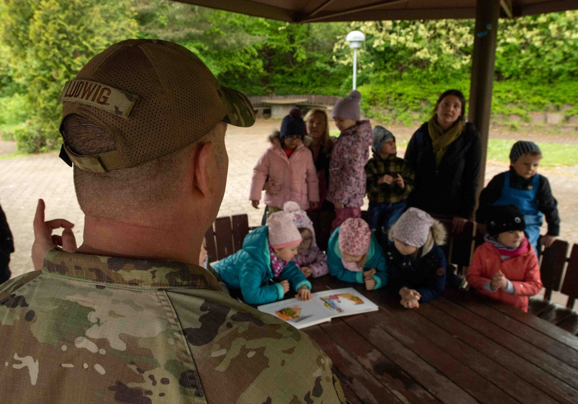 U.S. Air Force Chief MSgt. Ludwig , 86th Airlift Wing command chief, speaks to German children as they look at an English book during a Villa Winzig tour, Apr. 18, 2024. Ludwig read to children as part of an 86th Airlift Wing Host Nation Office community outreach program, which aims to enhance relations within the local community and introduce the English language to German children at an early age. (U.S. Air Force photo by Airman Dylan Myers)
