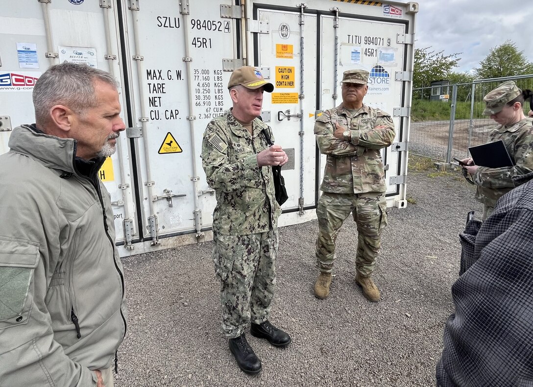Kevin Kachinski and Navy Rear Adm. Doug Noble address service members in front of shipping containers