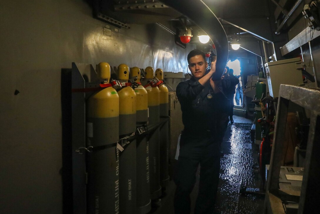 Sailors lift a hose inside a Navy ship during a wash down.