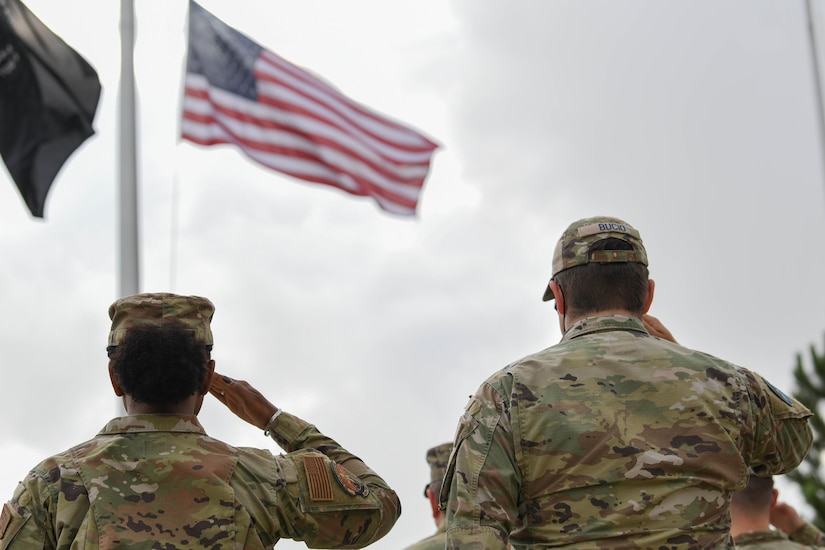 An airman and guardian salute as they face the American flag.