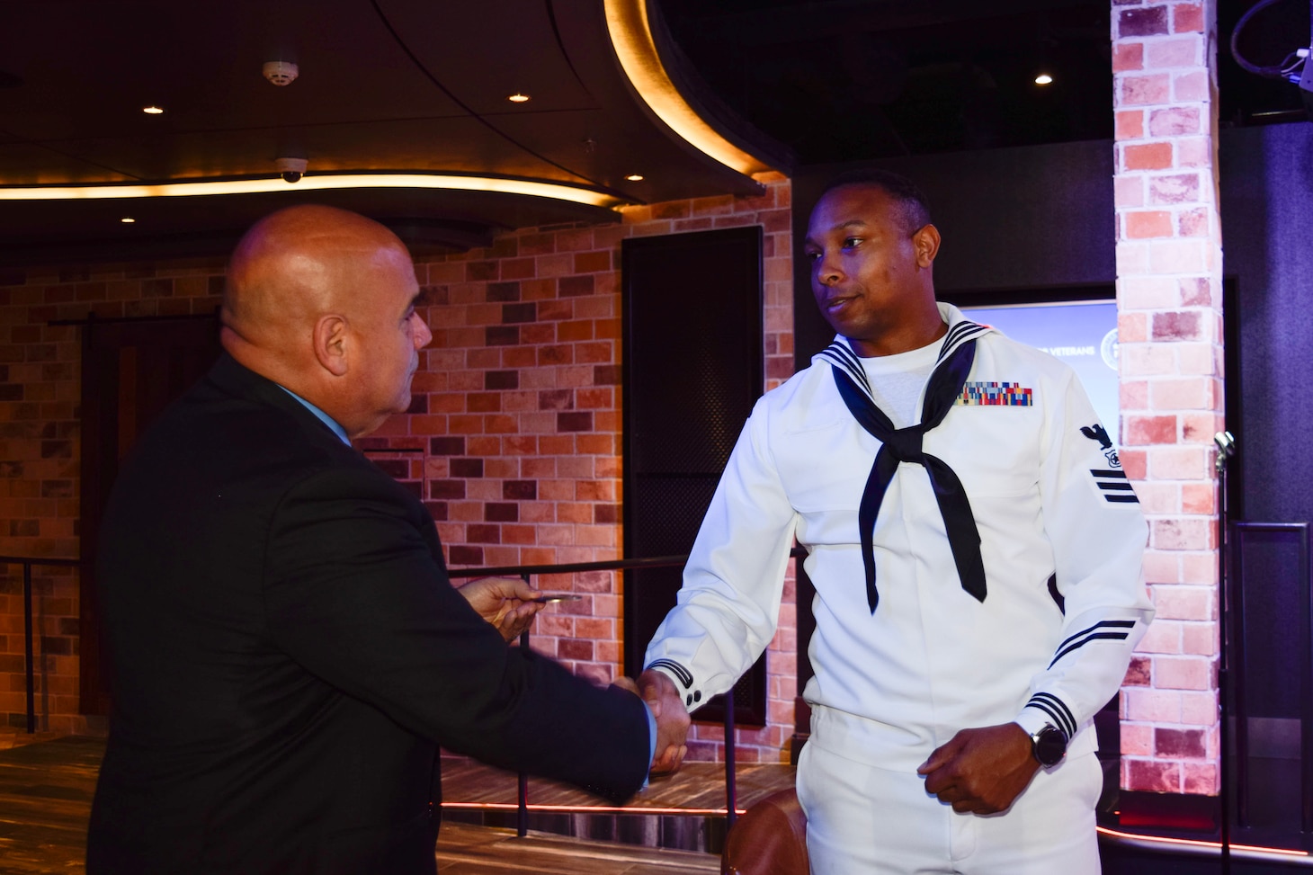 231108-N-RF885-1066 MIAMI (Nov. 8, 2023) - Master-at-Arms 1st Class Andrew Williams, a member of the Navy Reserve Center, Miami Color Guard, right, receives a coin from Norwegian Cruise Line’s (NCL) President, David Herrera, for his participation in a reception honoring Gold Star families aboard the Norwegian Joy, a Breakaway Plus-class cruise ship, docked in the Port of Miami, Nov. 8, 2023. NCL along with Honor and Remember, a non-profit organization whose flag recognizes the sacrifice of fallen heroes' families, have teamed up to fly their memorial flags across the 18-ship fleet. NRC Miami generates mobilization readiness in support of Joint Forces deployed globally by providing Reserve Component expertise, administrative services, and training to over 550 Select Reservists.(U.S. Navy photo by Mass Communication Specialist 1st Class Natalia Murillo/released)
