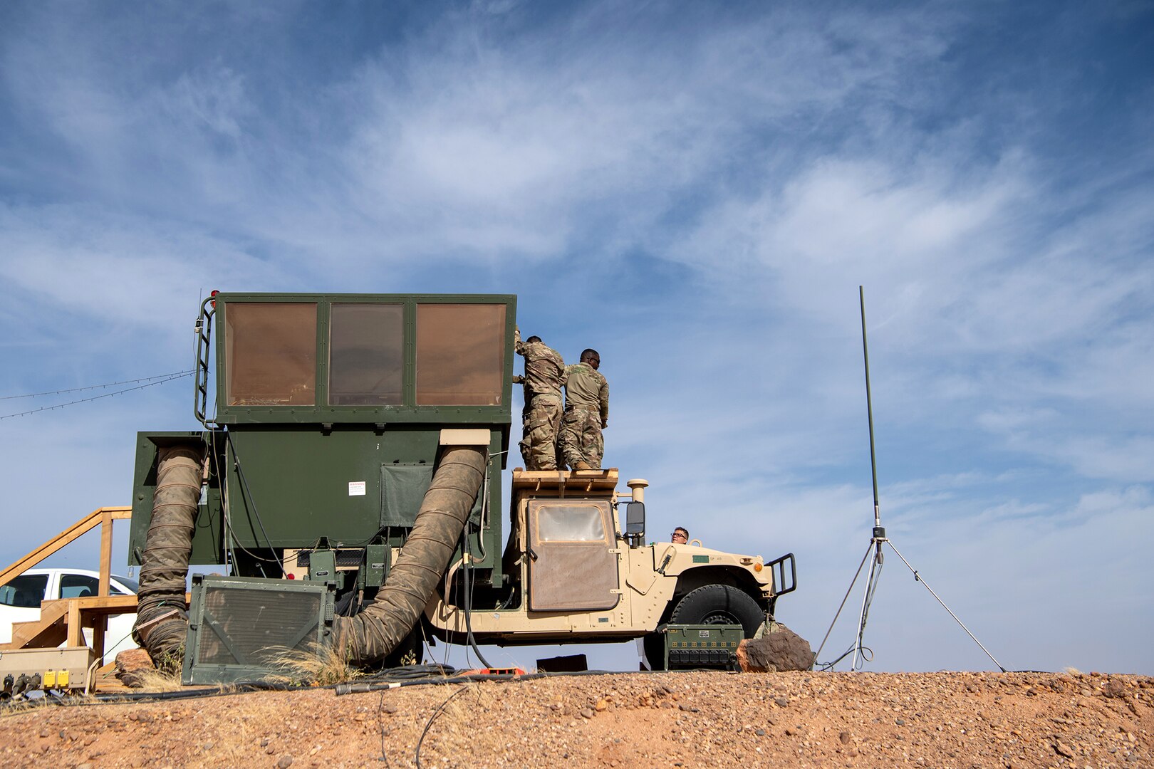 Three people stand on the roof of the cab of a Humvee to secure a panel to the vertical extension from the bed of the truck.