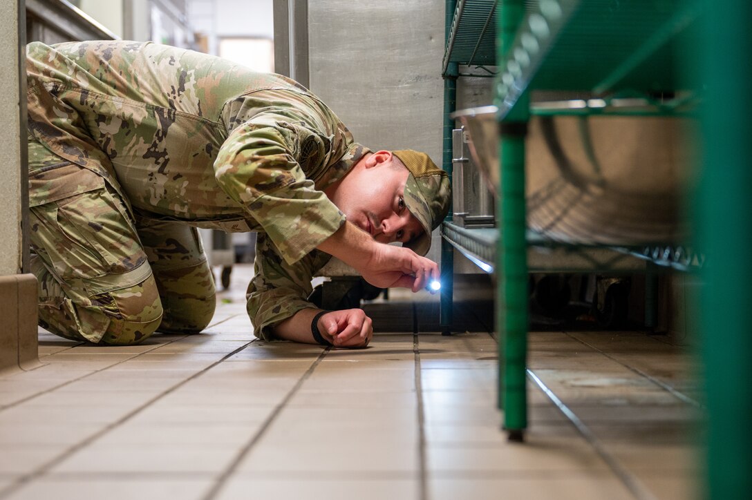 U.S. Air Force Senior Airman Christopher Cauldwell, 633d Civil Engineer Squadron pest management journeyman, searches for food and standing water on the ground of a food establishment on Joint Base Langley-Eustis, Dec. 4, 2023. Ensuring the absence of food or standing water is a preventive measure, as failure to address these issues promptly may attract pests. (U.S. Air Force photo by Airman 1st Class Skylar Ellis)