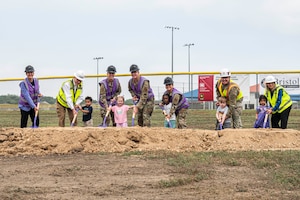 Seven adults and five kids pose with shovels on a line of dirt.