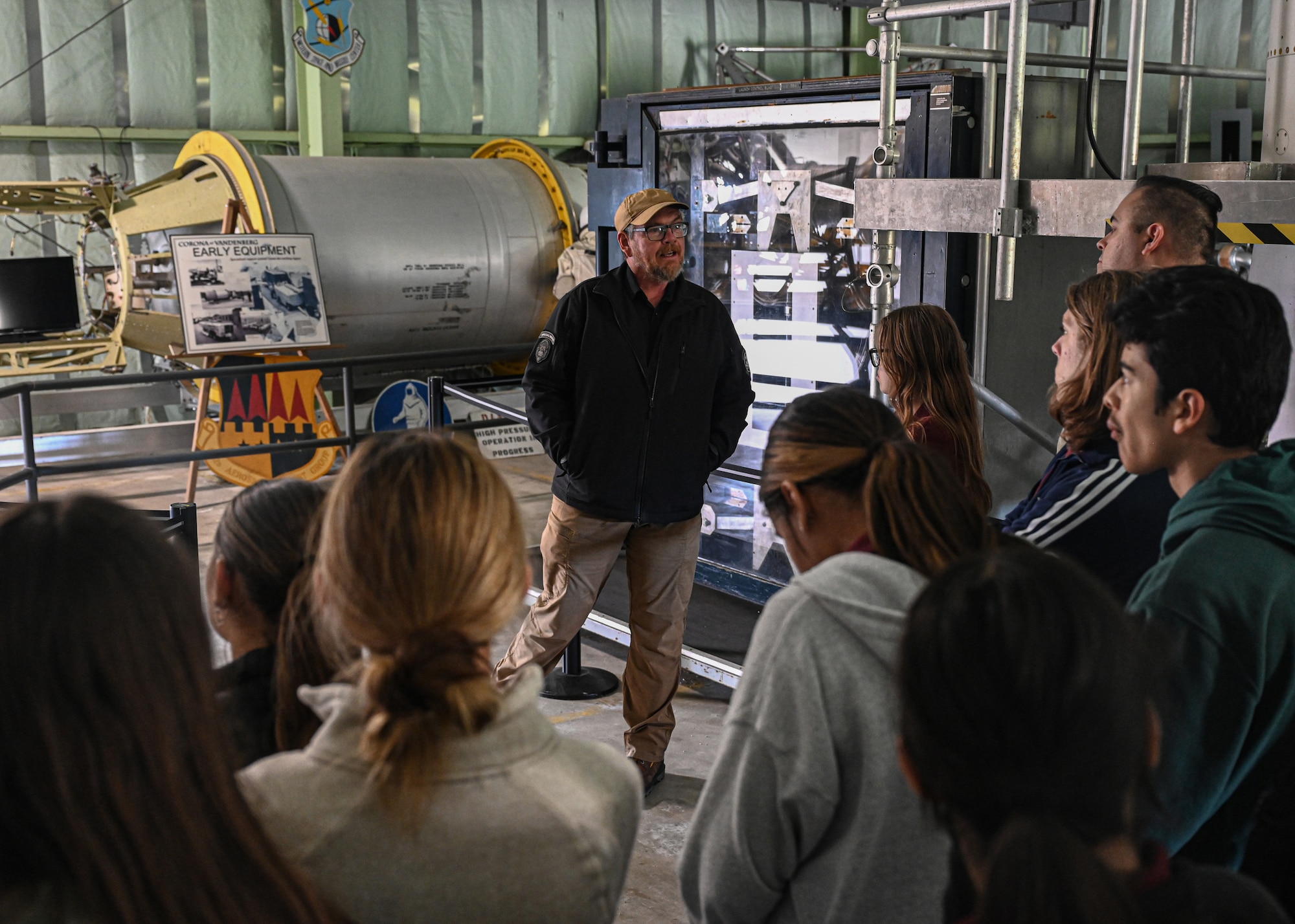 Man speaks to a group of students inside a museum.