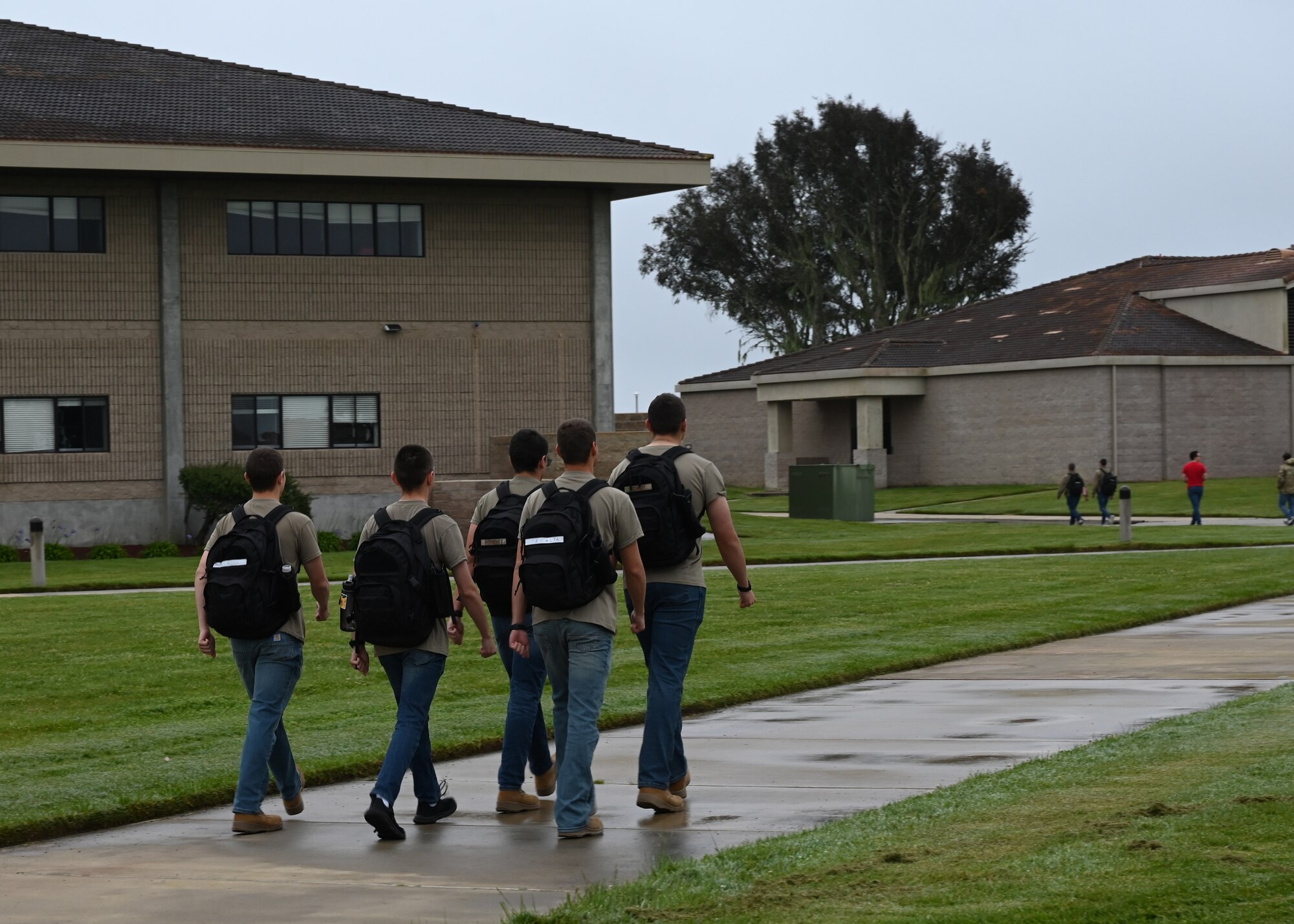 A group of students march in a formation on a sidewalk outside.