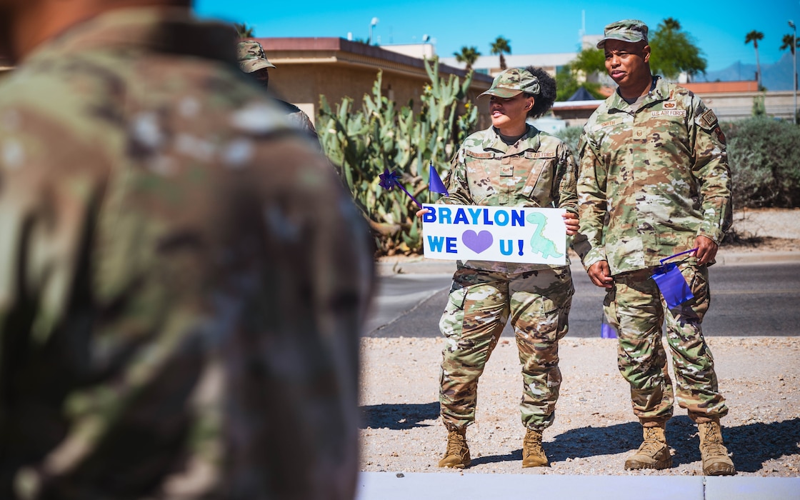U.S. Air Force Staff Sgt. Britni Thornton, 56th Medical Group non-commissioned officer in charge of core laboratory operations (left), and Master Sgt. Keeland Smith, 56th Component Maintenance Squadron lead standardization crew chief hold a sign for their military child prior to a Purple Up parade.