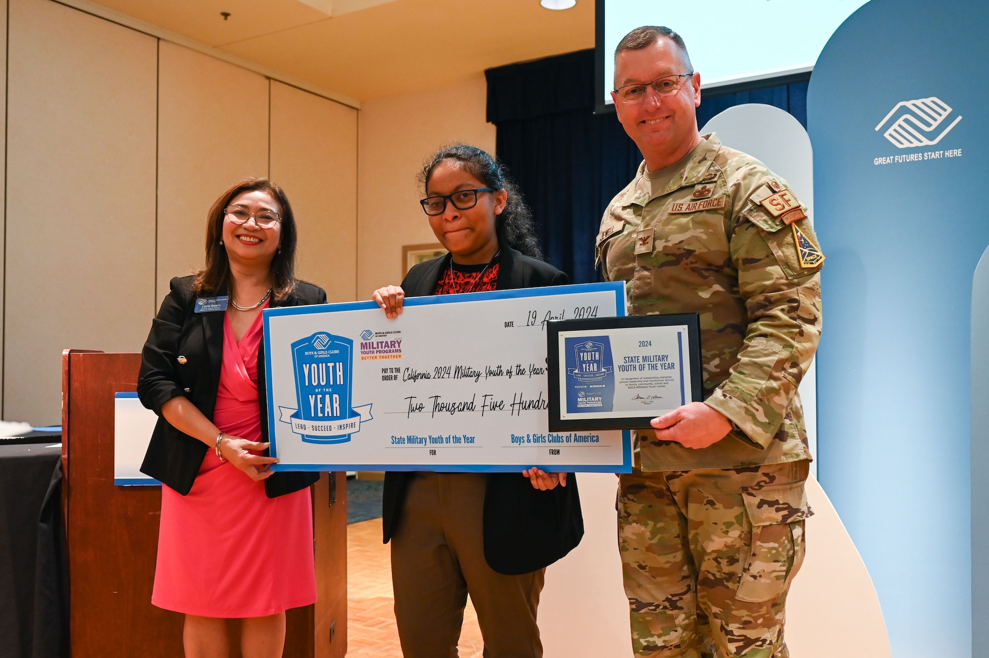 Three people pose with a large check and a plack.