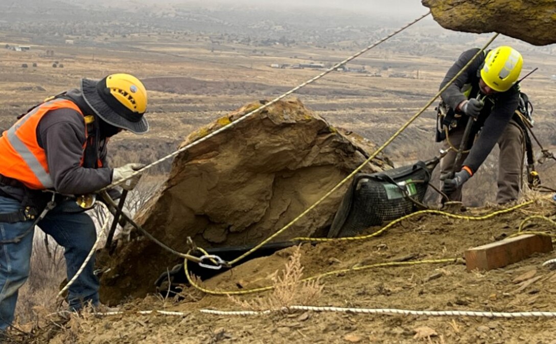 Workers move a boulder up the cliff face near the Farmer's Mutual Ditch. The boulder was moved to prevent it from being a rockfall hazard during the construction and installation phase of the project.