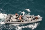 Four Marines operate a large inflatable boat in the ocean.