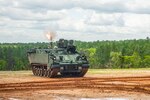 Soldiers fire a mortar from a tank in a large dirt field.