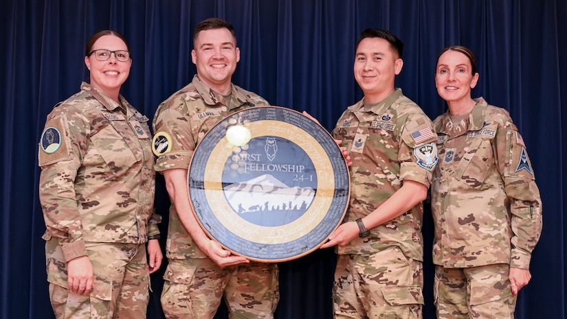 Four service members stand for a photo; the two in the center hold up a circular plaque.
