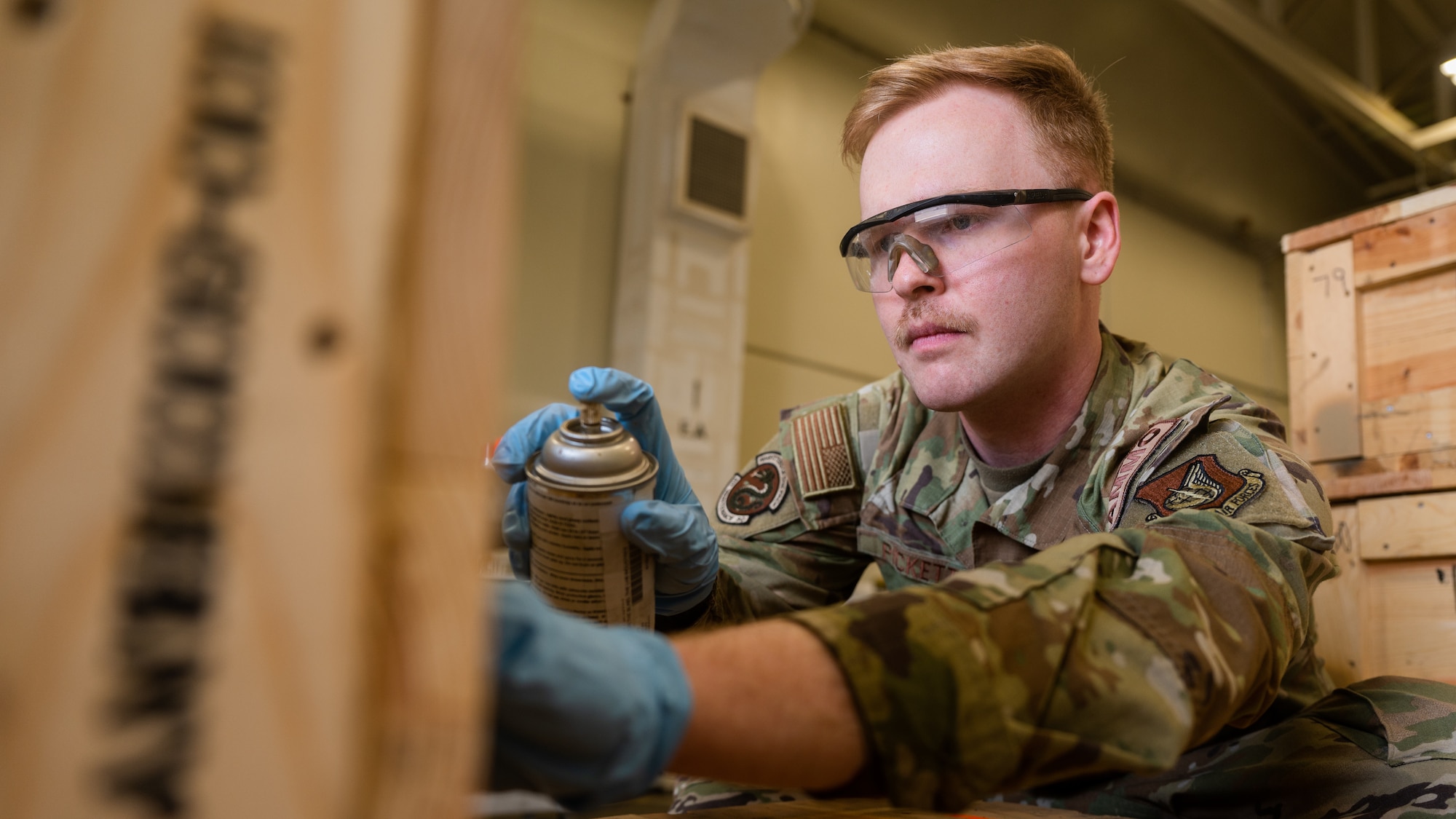 Senior Airman Ian Pickett spray paints a label on a box of ammunition.