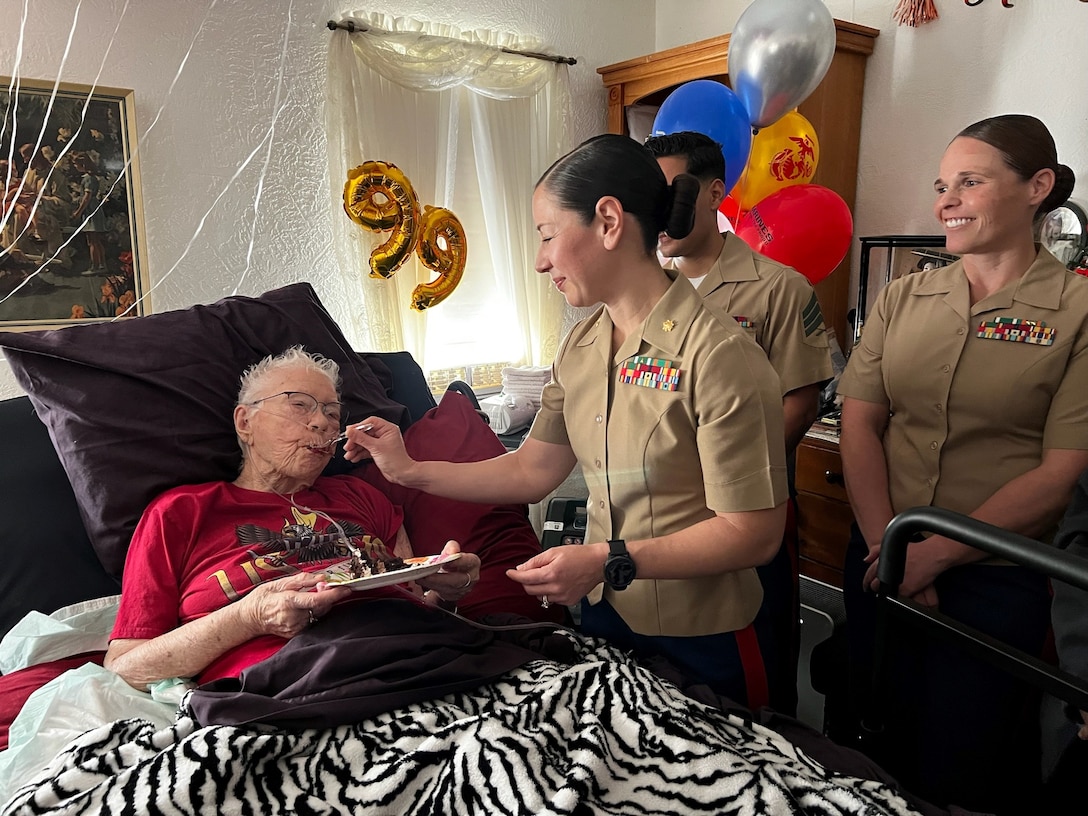 U.S. Marine Corps Major Shannon Potts, a Manpower Officer assigned to Headquarters Company, 23rd Marine Regiment, 4th Marine Division helps retired U.S. Marine Corps Corporal Lou 'Mama Lou' Keller eat her birthday cake during Mama Lou's 99th Birthday celebration, March 30, 2024, in San Jose, CA. Mama Lou served in the Marine Corps during WWII and strives to continue to encourage the next generation of Marines.