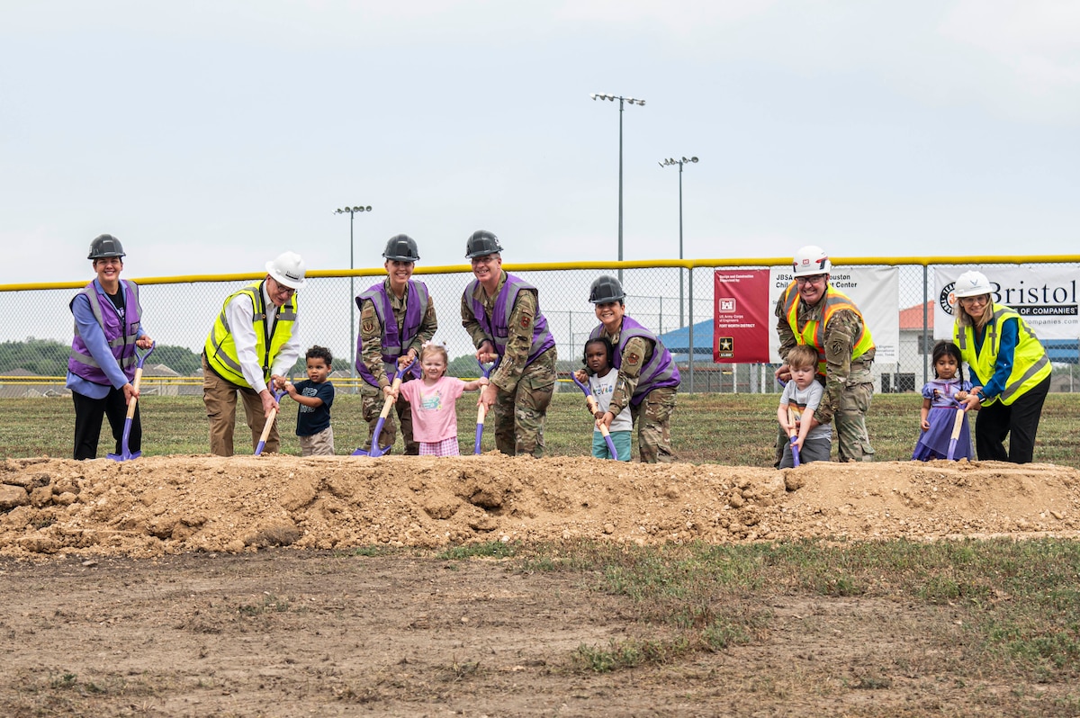 Seven adults and five kids pose with shovels on a line of dirt.
