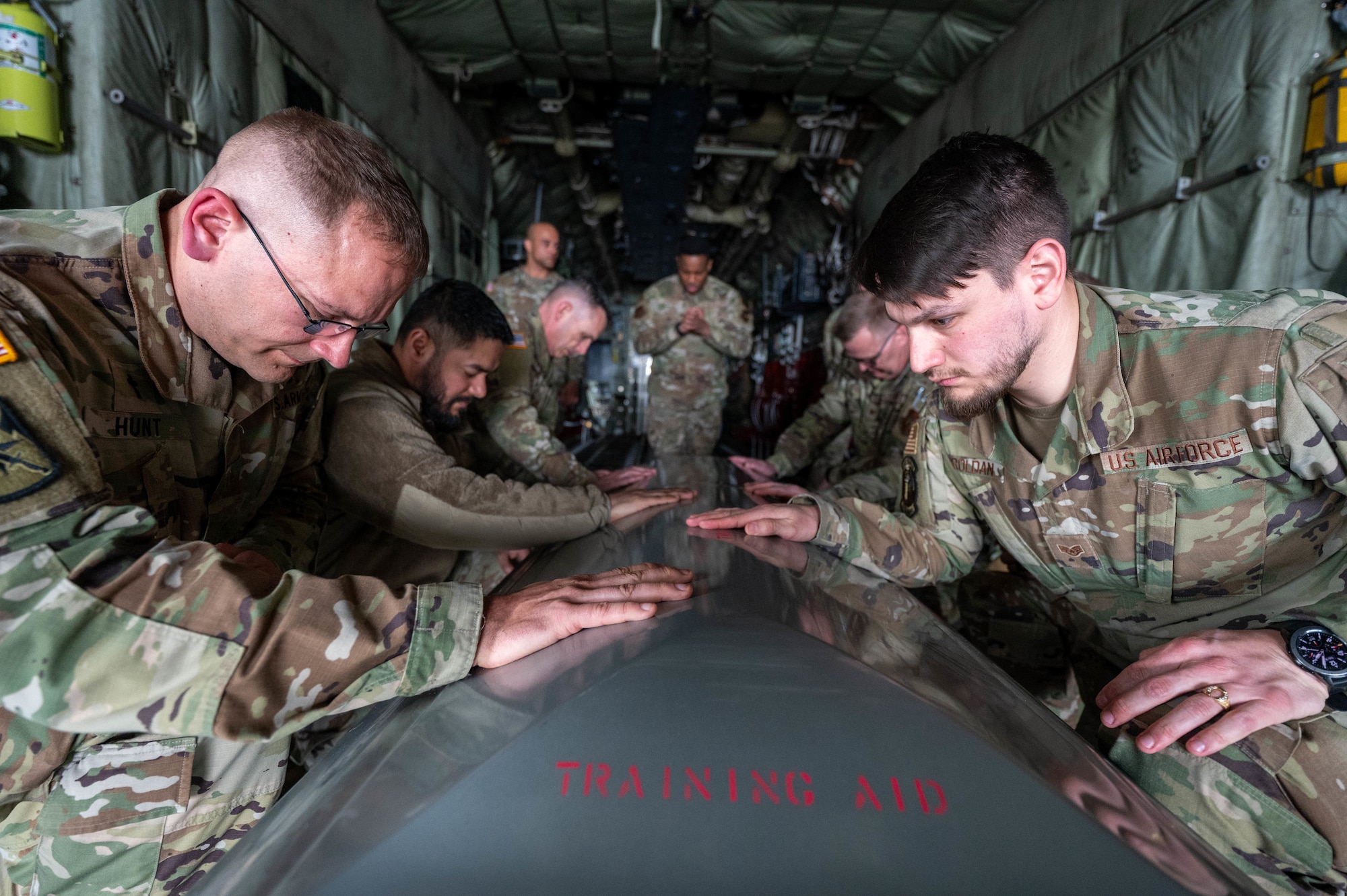 Religious support military members rest their hand on a training casket to say goodbye while a chaplain prays during a simulated ramp ceremony