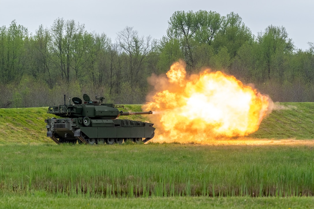 Flames erupt after a tank fires a mortar round in a large field.